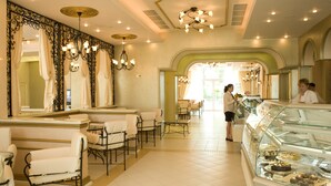 A hotel lobby with a reception desk, seating area, and a glass display case with desserts. - Sunset Resort (Pomorie)