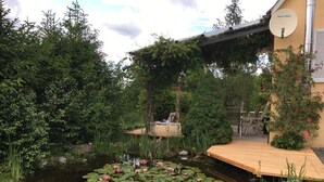Un jardin paisible avec un étang, une terrasse en bois et une végétation luxuriante.