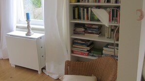 Une pièce avec une bibliothèque, un fauteuil en osier, un bureau et une fenêtre avec des rideaux.