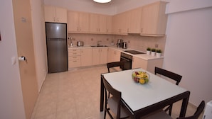 A compact kitchen with light wooden cabinets, a stainless steel refrigerator, a sink, and a dining table with chairs. - Keratea Apartment Athens Airport (Lavreotiki)