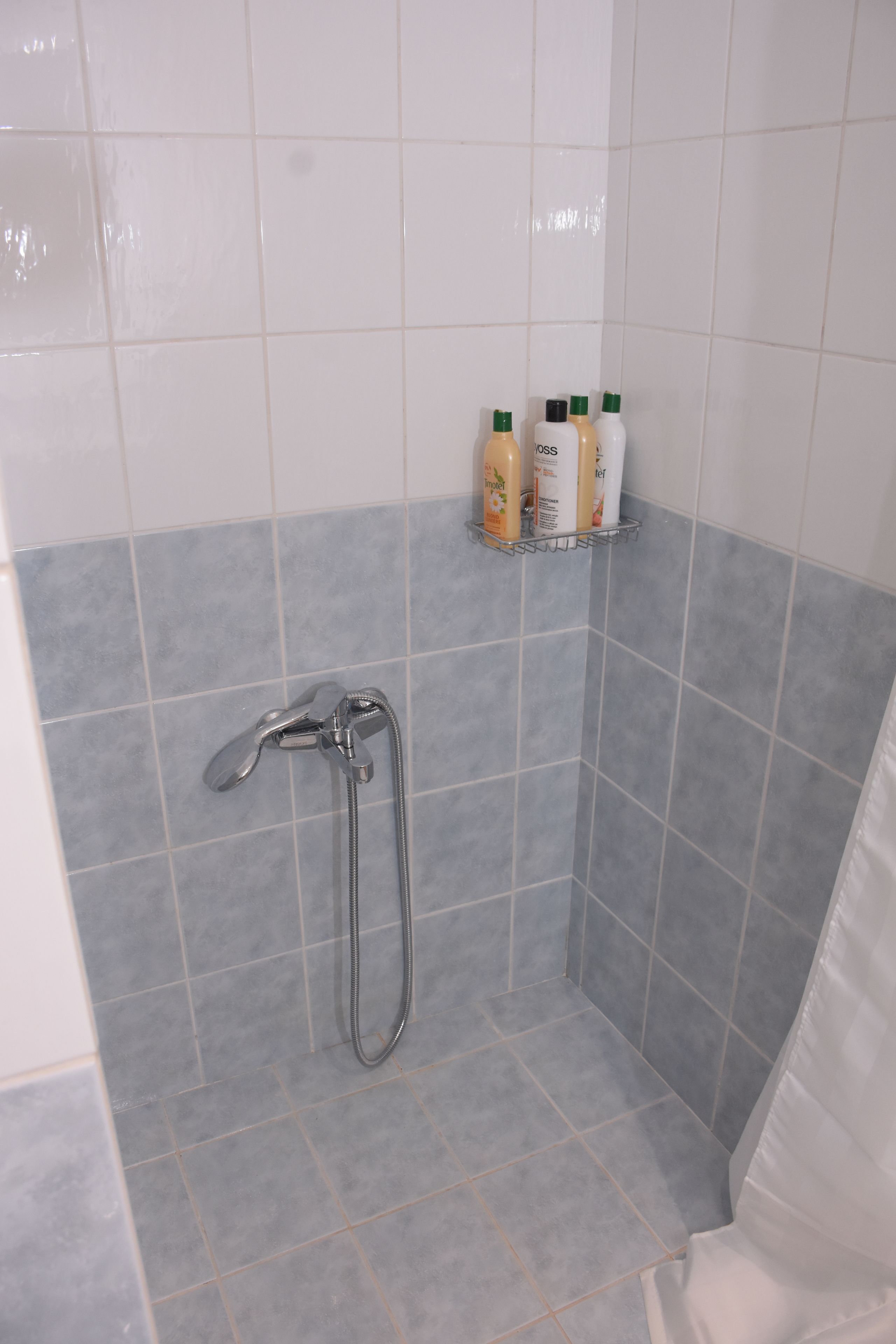Zona de ducha con azulejos grises, cabezal de ducha de mano y estante con artículos de aseo.