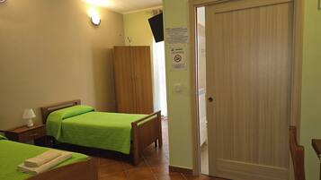 A hotel room with two beds, a wooden wardrobe, a door, and a wall-mounted light fixture.