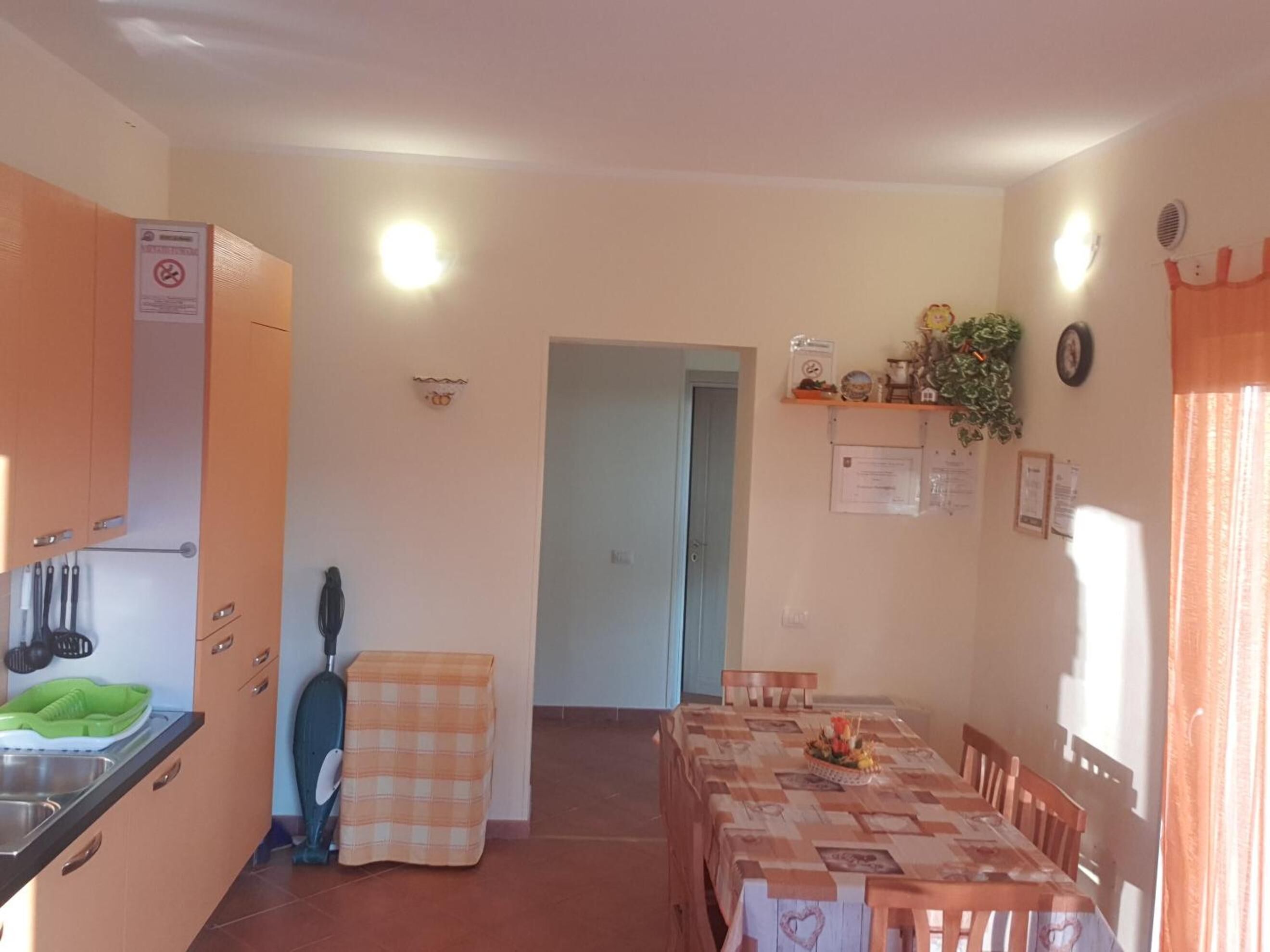 A compact kitchen with a sink, cabinets, and a checkered cloth. A dining area with a table and chairs is visible, and a door leads to another room.