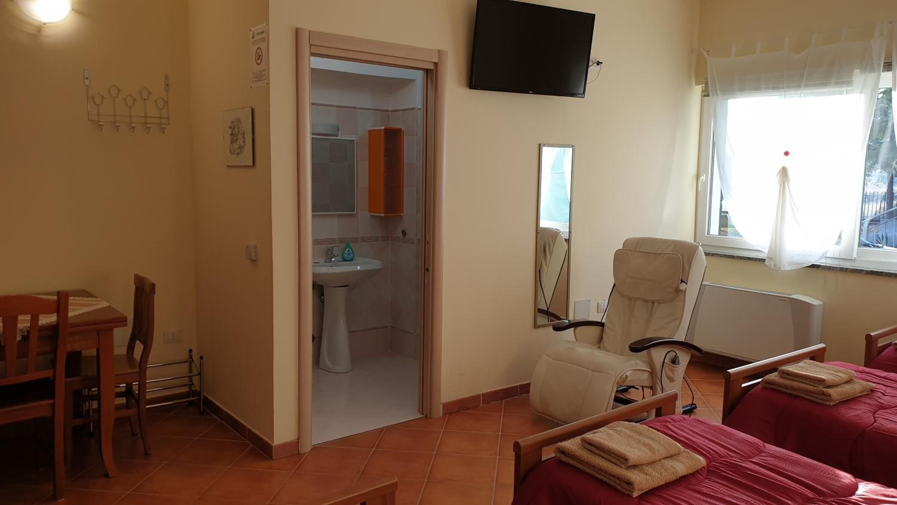 Una habitación con cama, una silla, un televisor y una ventana con cortinas.