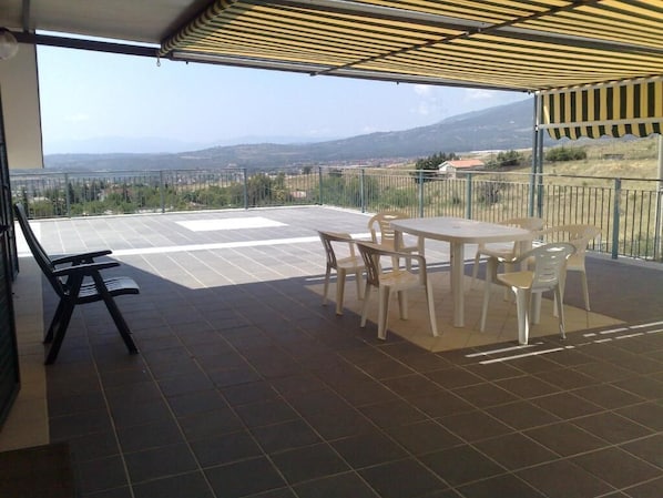 A covered outdoor patio with a table and chairs, a bench, and a view of the landscape. - B&B La Petrosa (Castrovillari)