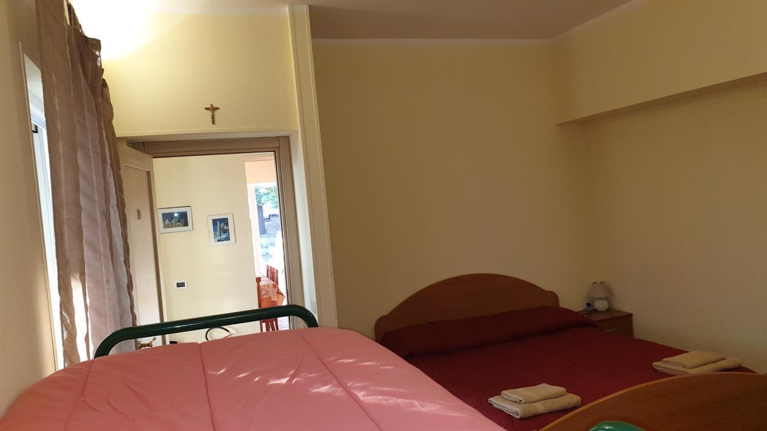 A bedroom with two beds, a wooden headboard, a small bedside table, and a cross on the wall.