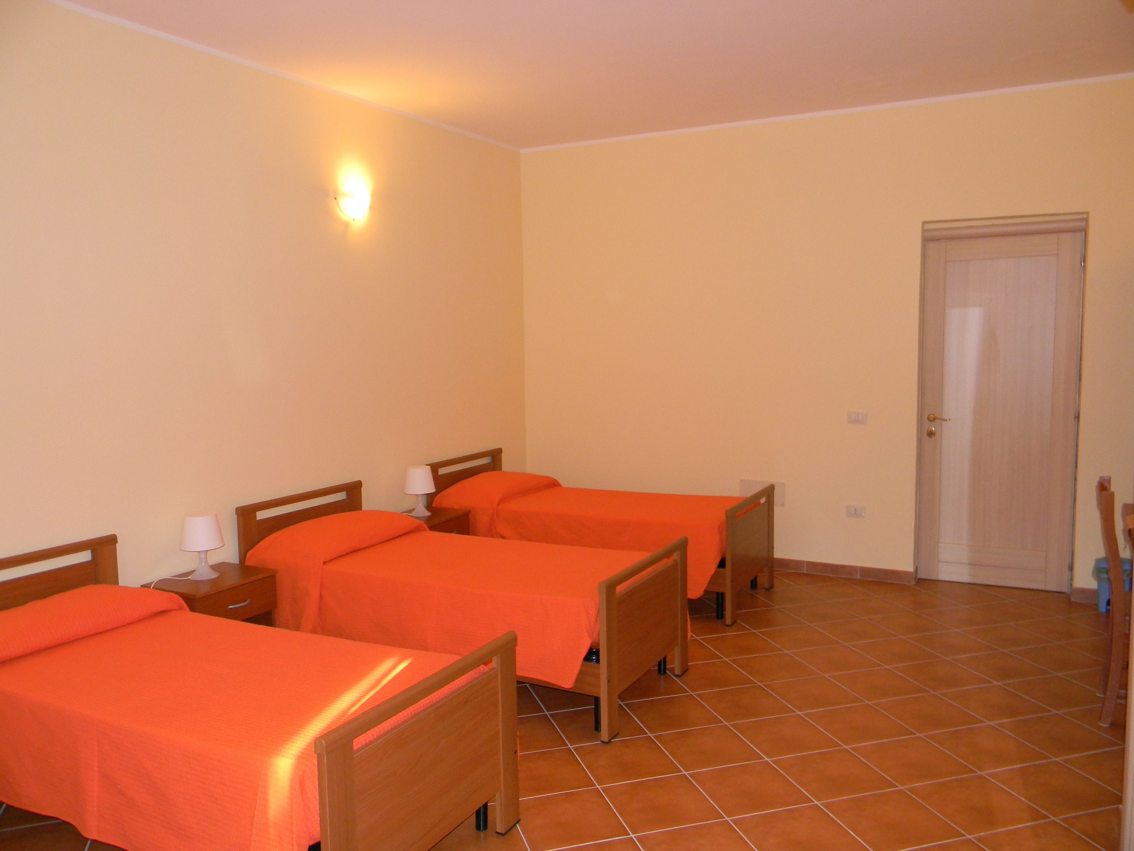 Habitación de hotel con tres camas de madera, cada una con una lámpara blanca a su lado.