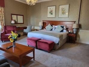 A hotel room with a large bed, two bedside tables, a wooden desk, a red armchair, and a chandelier. - Leixlip Manor Hotel (Leixlip)