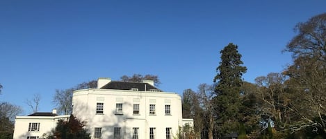 A large, white, two-story building with a symmetrical facade, surrounded by a well-maintained lawn and trees.