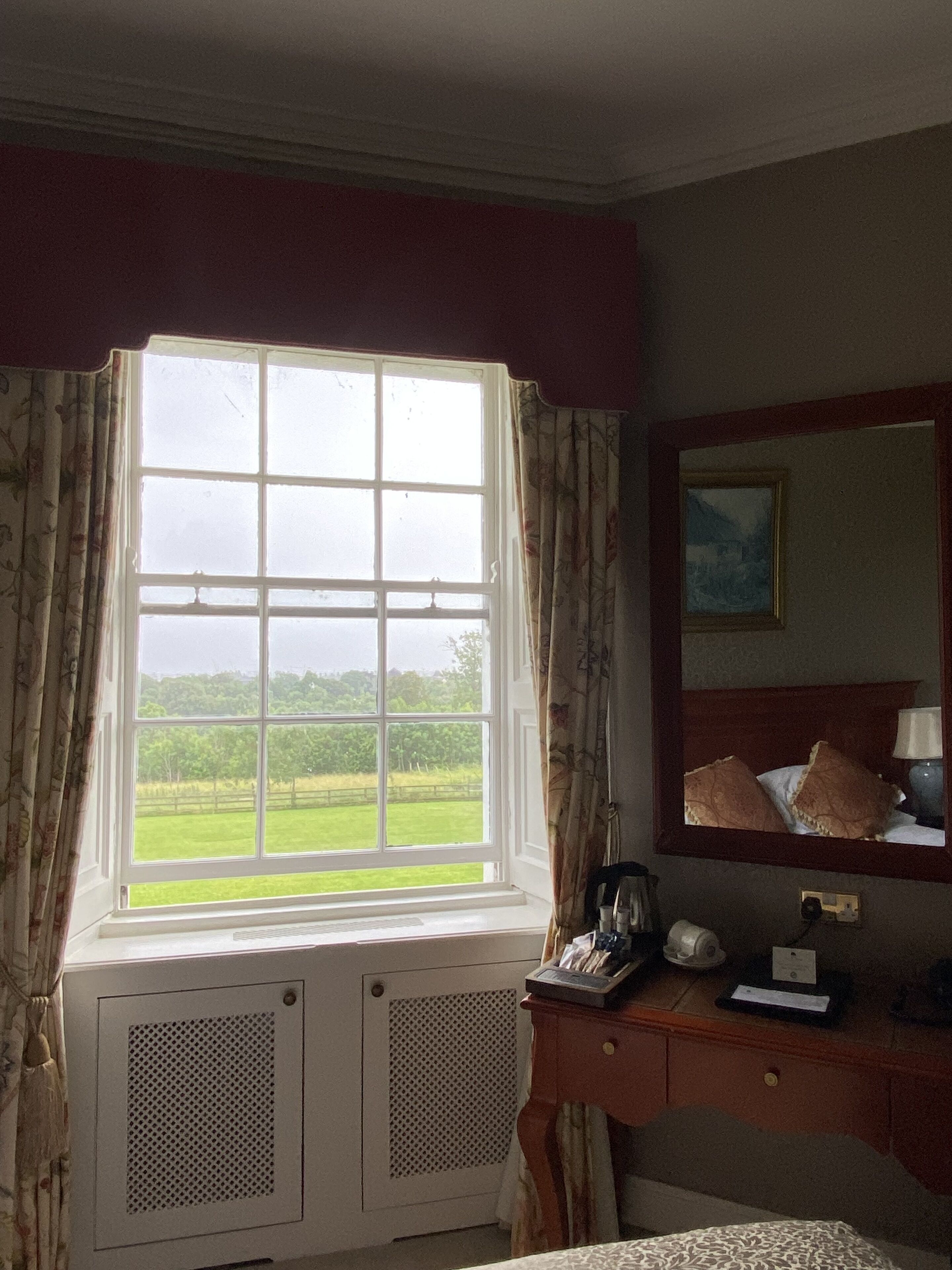 A room with a large window, a wooden dresser, a mirror, and a radiator.