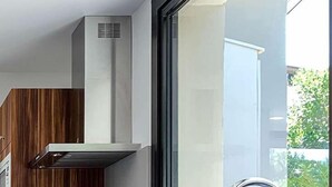 Une cuisine moderne avec des meubles en bois, une hotte en acier inoxydable et une grande fenêtre avec un évier.