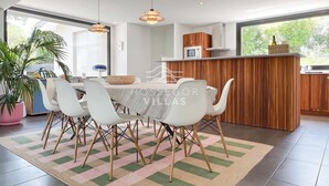 Une cuisine moderne avec un coin repas, comprenant un grand îlot central, des chaises blanches et des luminaires suspendus.