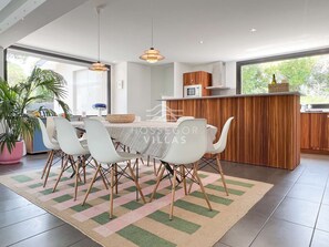 A modern kitchen with a dining area, featuring a large island, white chairs, and pendant lighting.