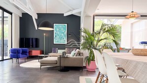 Un salon moderne comprenant un canapé, une table basse, une table à manger avec des chaises, une grande plante en pot et un tableau accroché au mur.