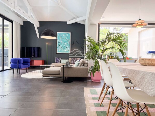 Un salon moderne comprenant un canapé, une table basse, une table à manger avec des chaises, une grande plante en pot et un tableau accroché au mur.