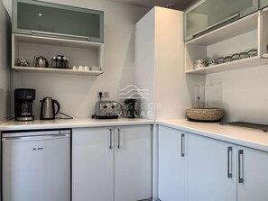Une cuisine moderne avec des meubles blancs, une machine à café, un grille-pain et un mixeur posés sur le plan de travail.