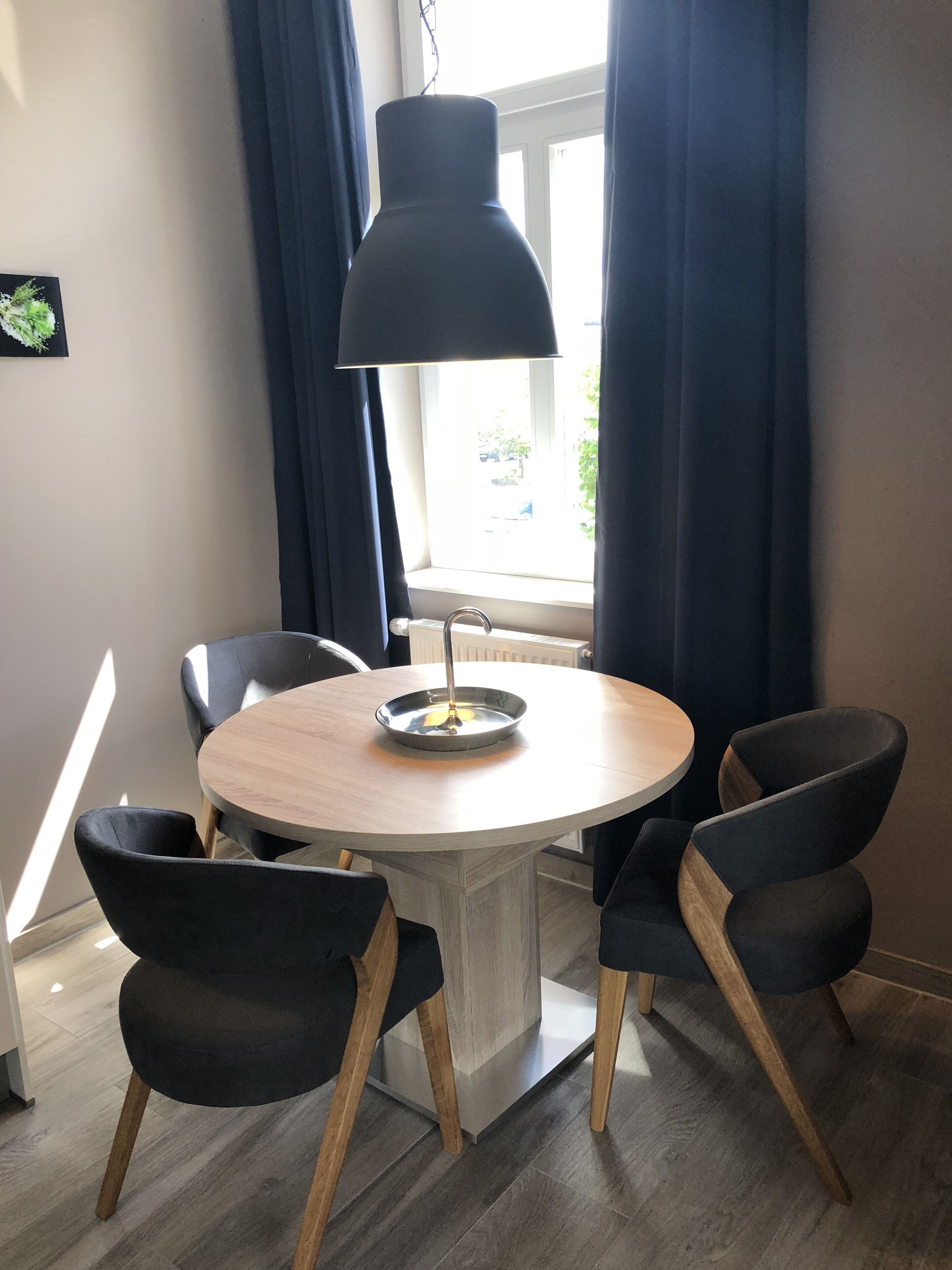 A dining area with a round table, four chairs, a lamp, and a window with curtains.