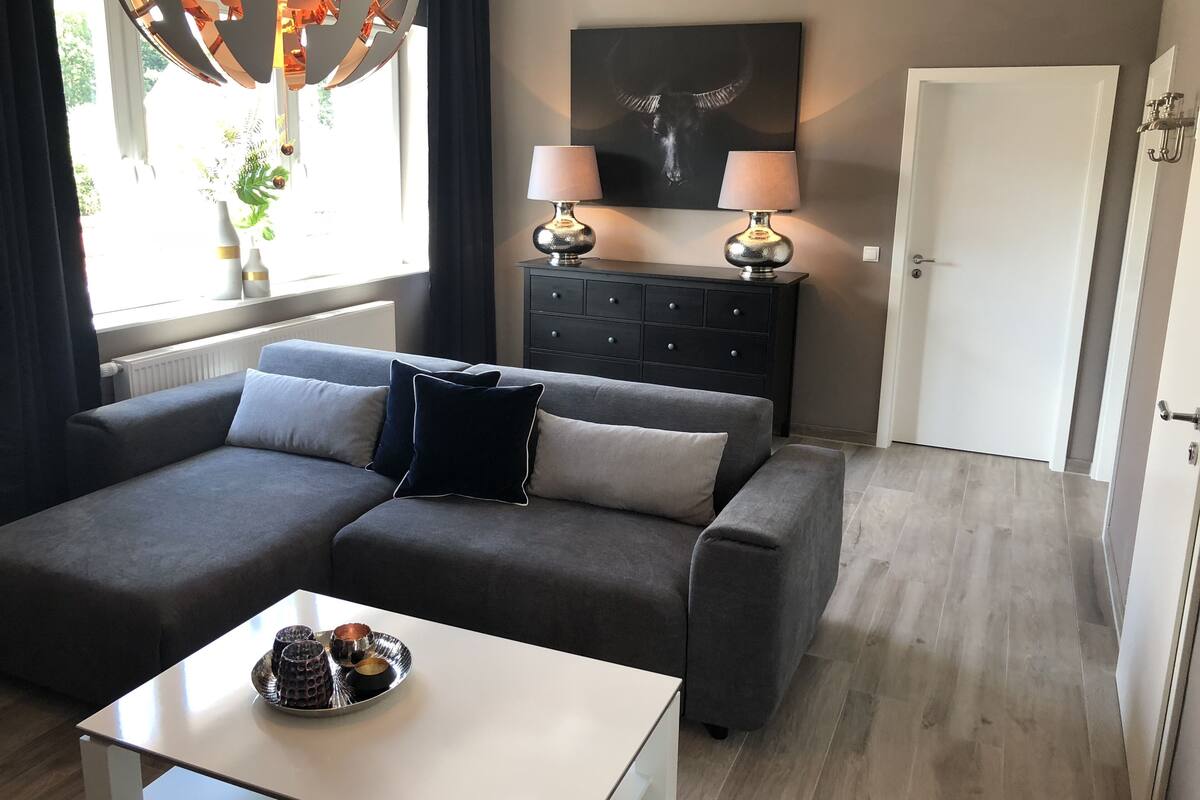 A modern living room with a grey sofa, two lamps, a coffee table, and a painting on the wall.