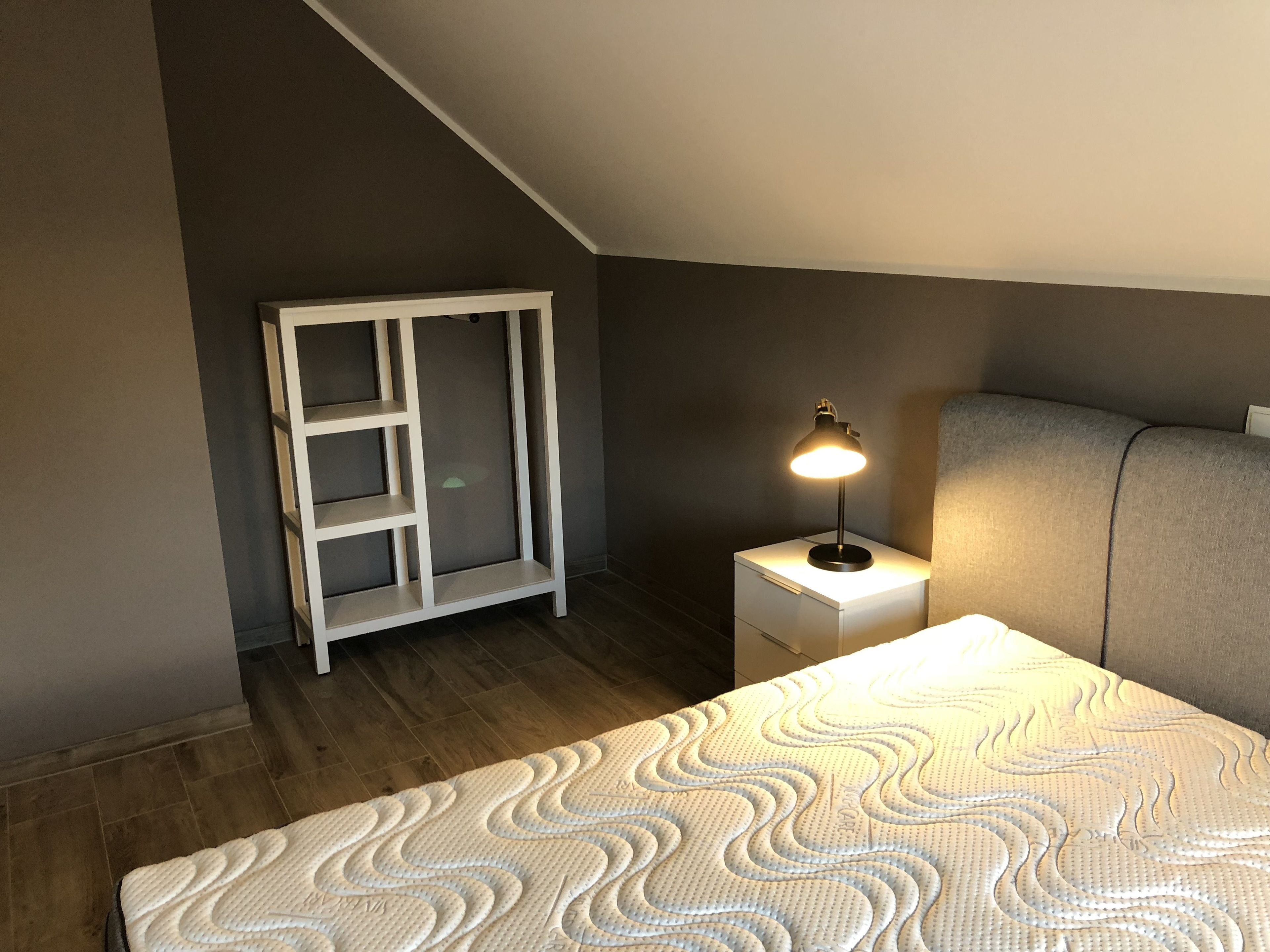 A bedroom with a bed, a nightstand, a lamp, and a wardrobe.