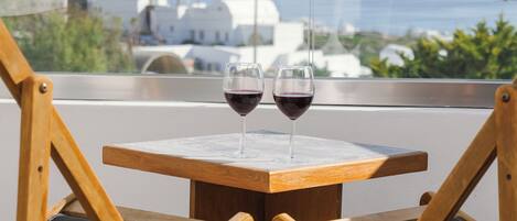 Una mesa de madera con dos copas de vino tinto, vista al mar y edificios blancos al fondo.
