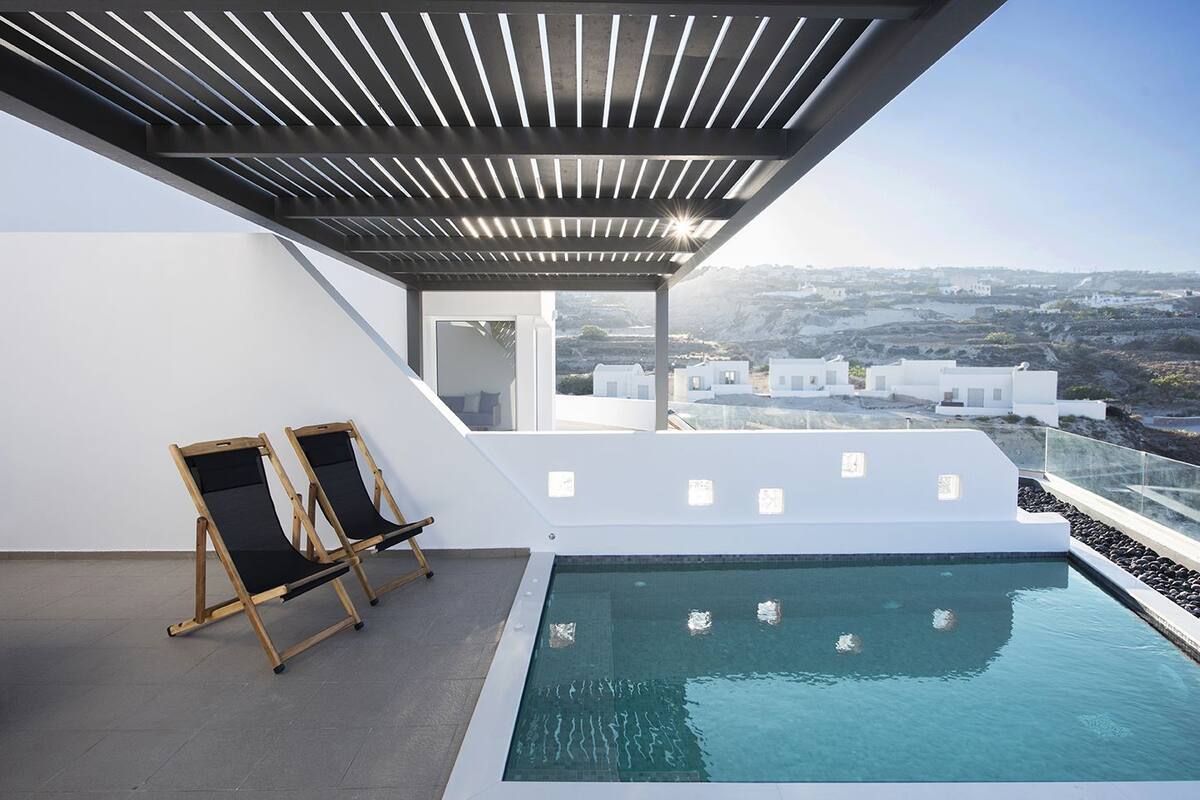 Una piscina infinita en la azotea con dos sillones de madera, una pérgola y vistas a edificios distantes.