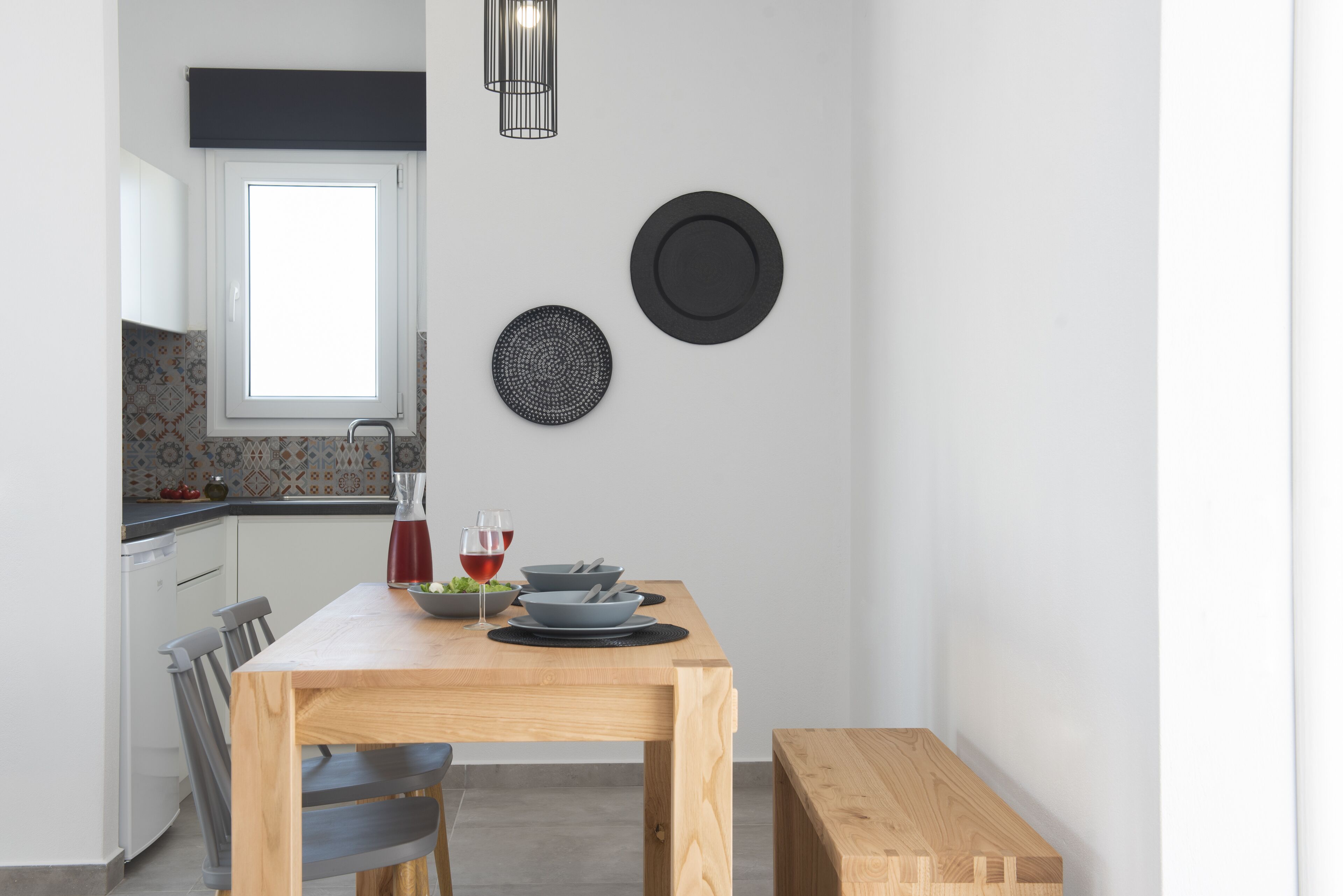 Een moderne keuken met een houten tafel, twee stoelen, een raam en een zwart hanglamp.