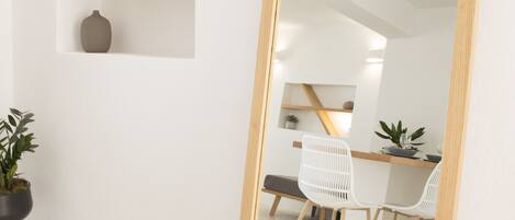 A room with a large mirror, a desk with two chairs, a potted plant, and a shelf with decorative items.