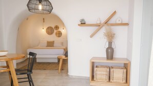 Un dormitorio acogedor con pared curva, una cama, una mesita de noche, una silla, una mesa de comedor de madera y un estante con objetos decorativos.
