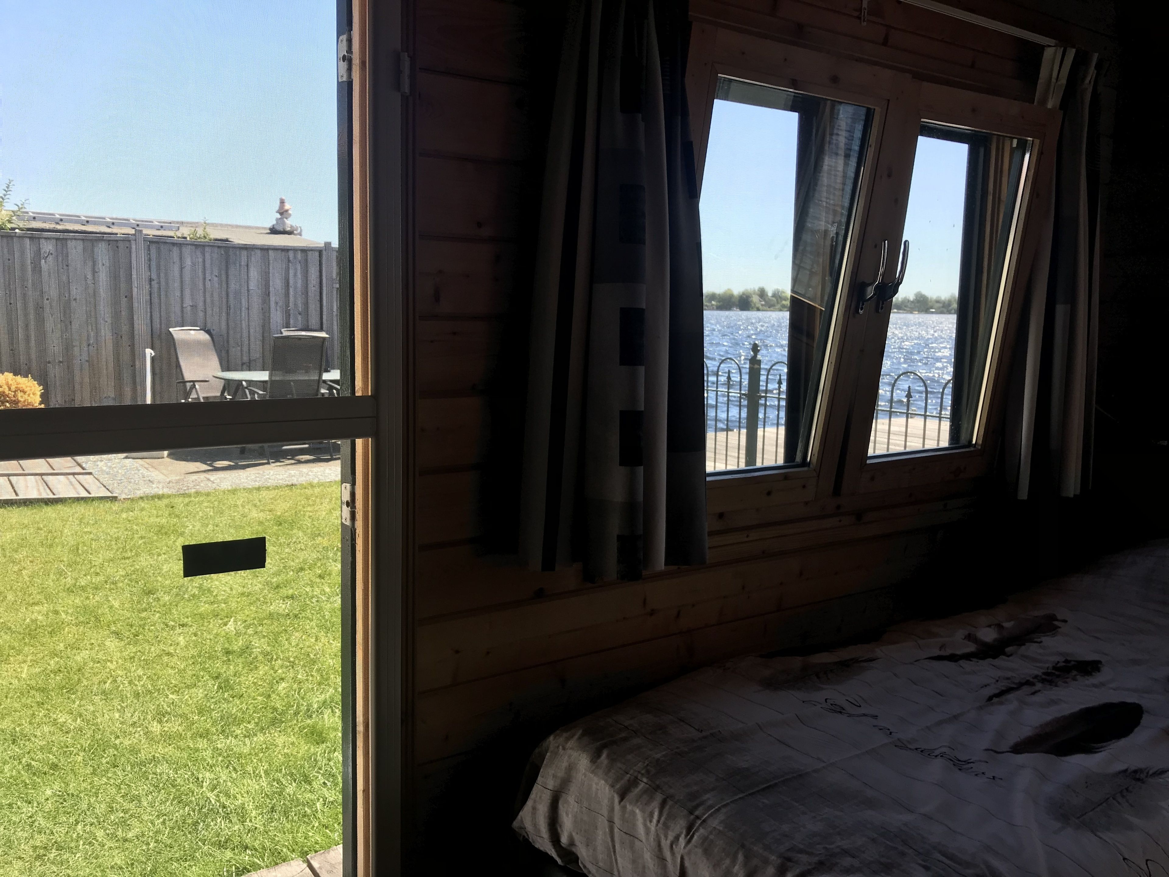 A room with a bed, a window with curtains, and a view of a body of water and outdoor furniture.