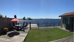A backyard with a wooden deck, a red umbrella, and a view of a lake. - Vvp Verhuur Visserslust Vinkeveen (Vinkeveen)