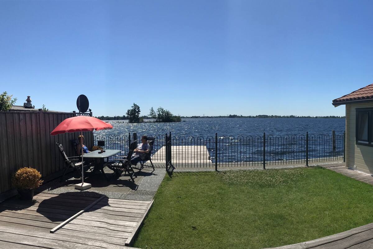 Un jardin avec une terrasse en bois, un parasol rouge et une vue sur un lac.