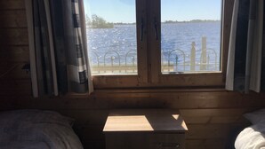 A cabin with a wooden interior, a window with metal bars, and a view of a body of water. - Vvp Verhuur Visserslust Vinkeveen (Vinkeveen)