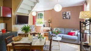 A modern living room with a sofa, dining table, and chairs. There is a staircase leading to an upper level. - Charming house in the valley for 2, nature and tranquility (Beauficel)