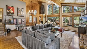 A spacious living room with a large gray sectional sofa, wooden ceiling, and large windows offering views of the outdoors. - Artist’s Haven – Stylish Dollar Point Home with Hot Tub Near Skylandia Beach (Tahoe City)