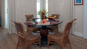 A dining area with a round glass table, wicker chairs, and a vase of flowers. - 3br Plantation at Princeville! AC, fitness center, hot tub,, garage, more! (Princeville)