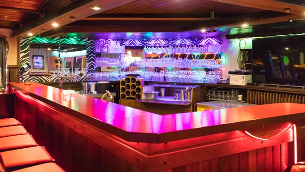 A bar area with a wooden counter, shelves of glasses, and a zebra-patterned wall. - Hotel Berlin (Schwetzingen)
