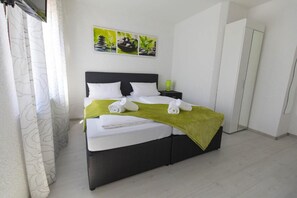 A neatly made bed with white linens and a green throw, a nightstand with a lamp, and a wall with three framed pictures. - Hotel Berlin (Schwetzingen)
