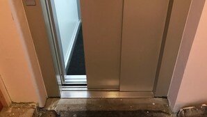 An elevator with a metallic finish, a control panel with a button, and a small sign. - Hotel Berlin (Schwetzingen)