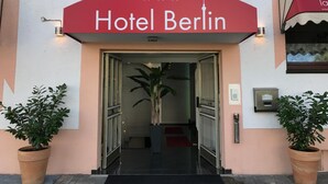 The entrance to Hotel Berlin with a red awning, a glass door, and potted plants on either side. - Hotel Berlin (Schwetzingen)