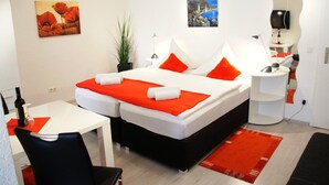 A hotel room with a bed, a desk, a chair, a TV, and artwork on the walls. - Hotel Berlin (Schwetzingen)