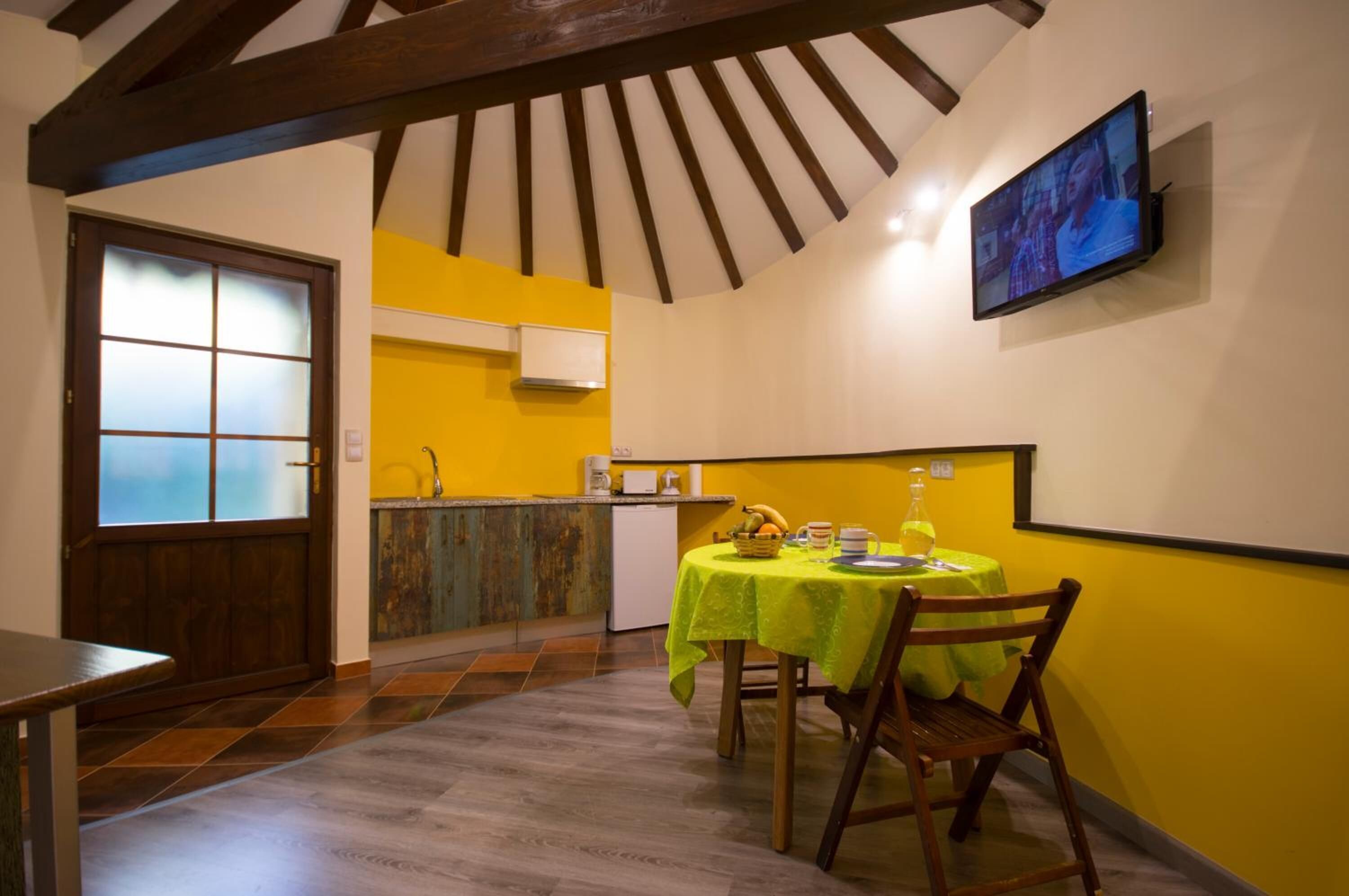 Un coin repas avec une table dressée pour deux personnes, une cuisine en arrière-plan et un téléviseur fixé au mur.