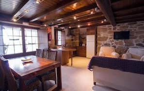 A cozy interior with a wooden dining table, wicker chairs, a sofa, and a kitchen area with stone walls. - Casa Rural O Canto da Terra (Panton)