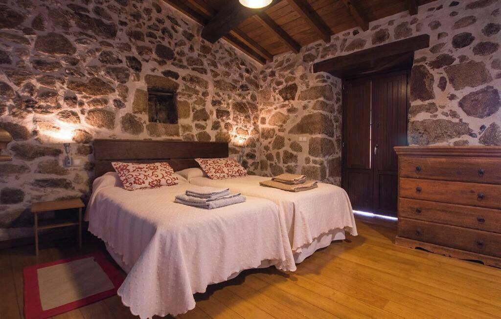 Een slaapkamer met stenen muren, een houten plafond, een bed met witte beddengoed, een dressoir en een nachtkastje.