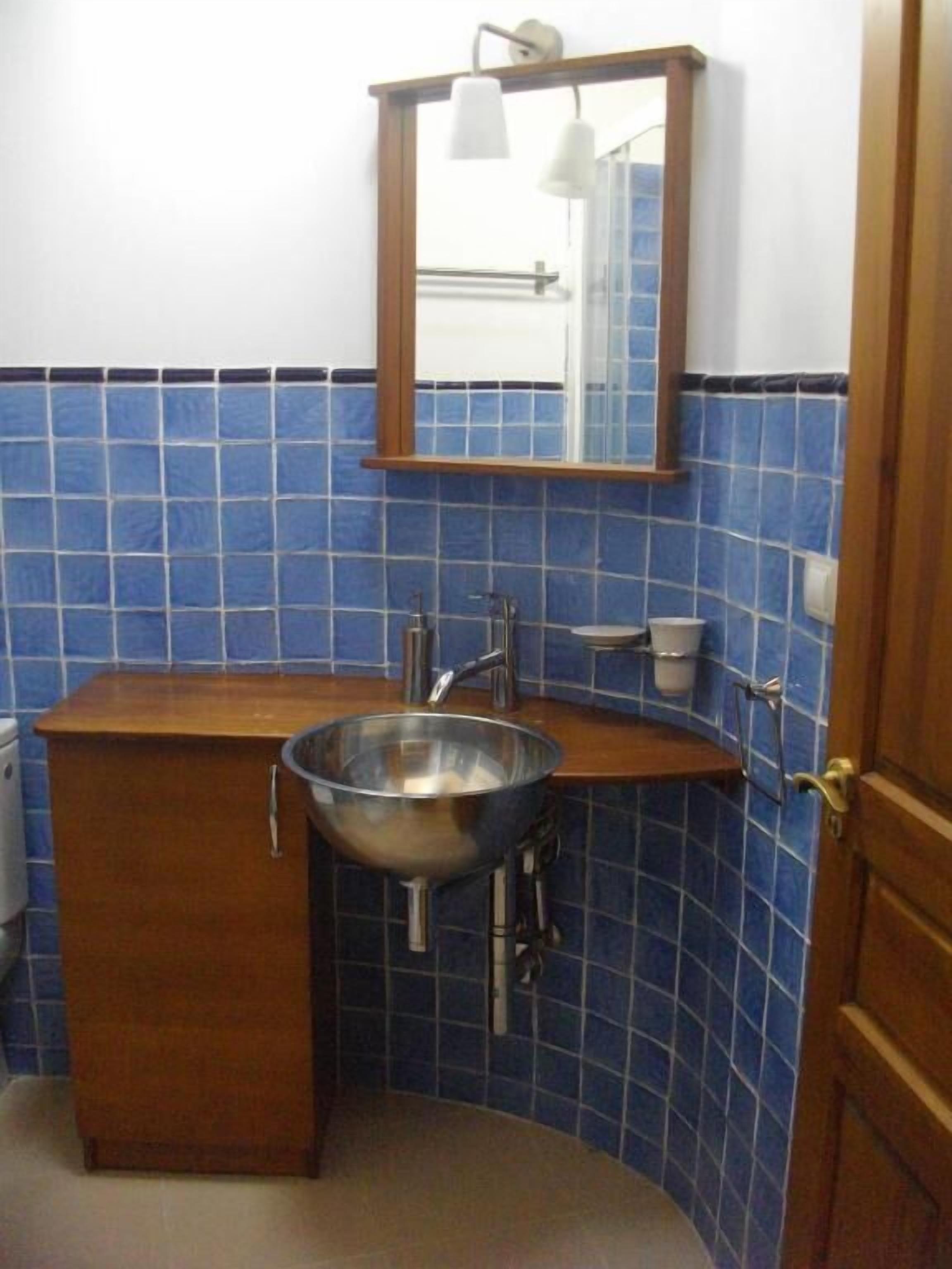 A bathroom with a wooden vanity, a stainless steel sink, and blue tiled walls.