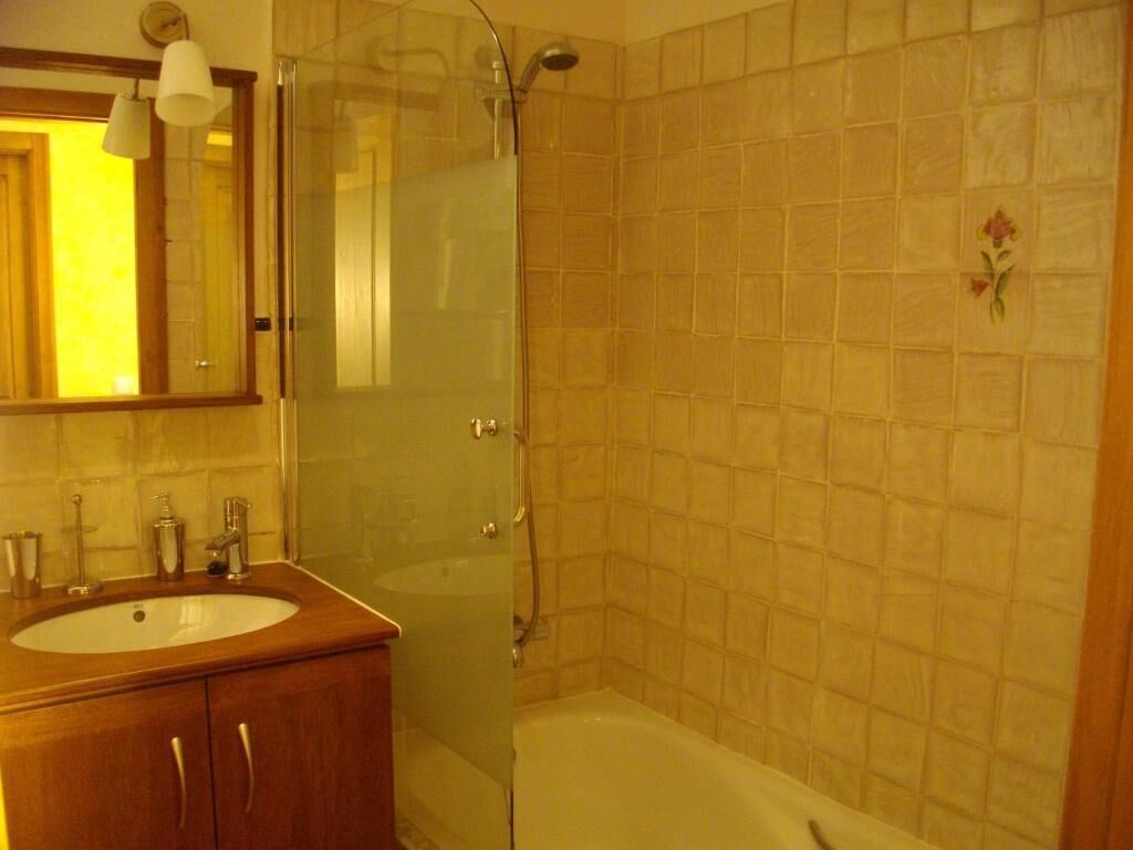 A bathroom with a wooden vanity, a glass shower enclosure, and tiled walls.
