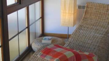 Una habitación con un ventanal grande, una silla de mimbre, una mesita redonda pequeña y una lámpara de pie alta.