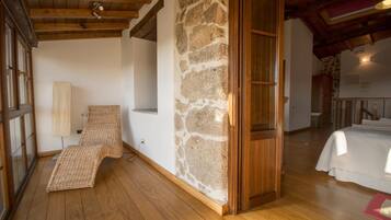 A room with a stone wall, wooden beams, a bed, and a window.