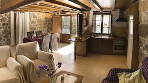 Ett mysigt vardagsrum med en soffa, ett matbord med stolar, en köksdel med diskho och spis samt en vägg av sten.