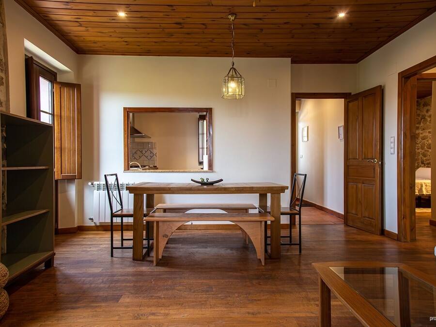 Un comedor con mesa y sillas de madera, una lámpara colgante y un espejo en la pared.