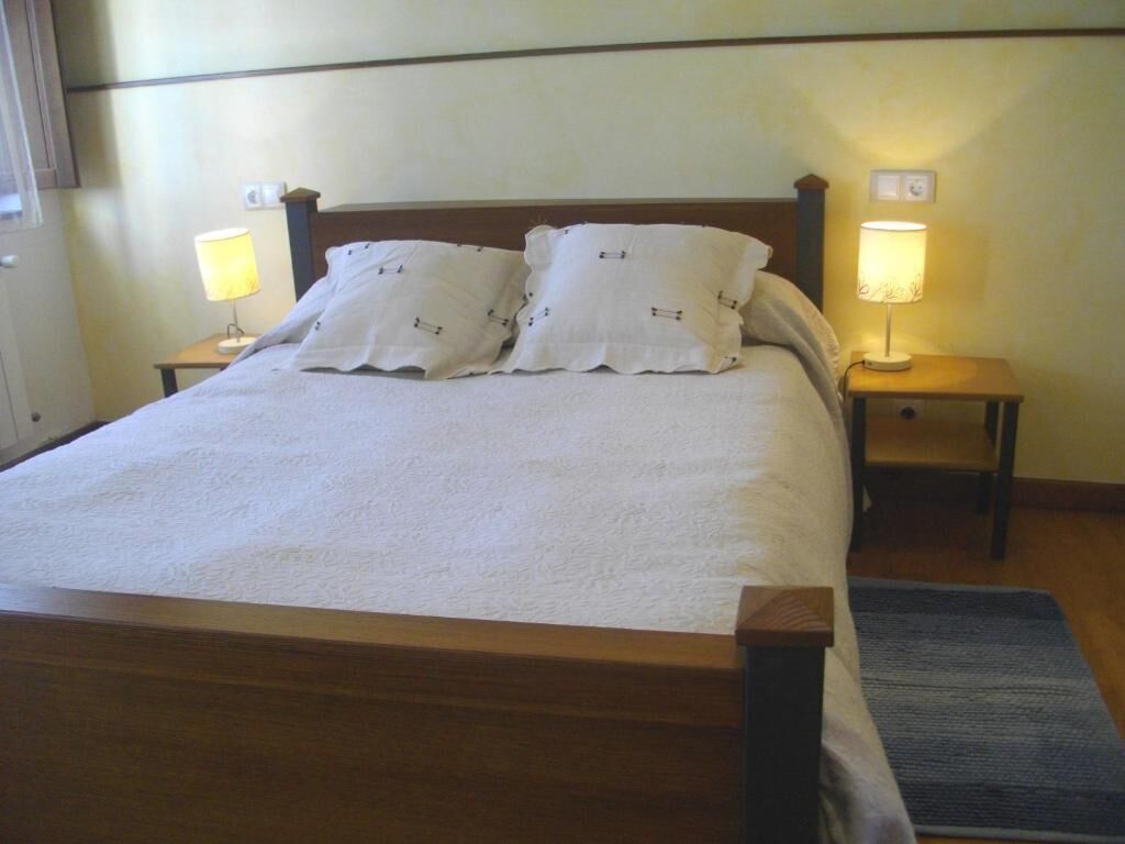 A neatly made bed with two pillows, two bedside lamps, and a wooden headboard.